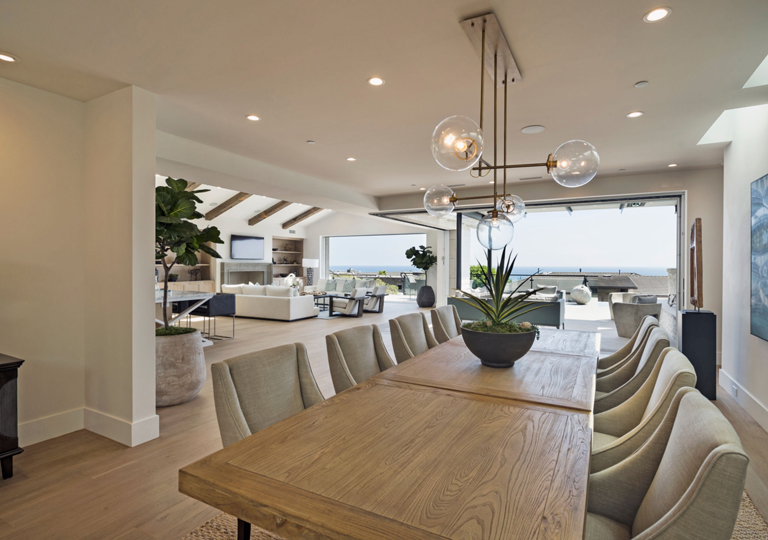 Comedor moderno con lámpara decorativa, vista al mar, techo con vigas y conexión abierta a sala integrada – FRANCO HomeServices