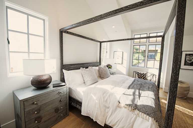Dormitorio de lujo con cama de dosel de madera oscura, amplio ventanal y mesita de noche moderna – FRANCO HomeServices