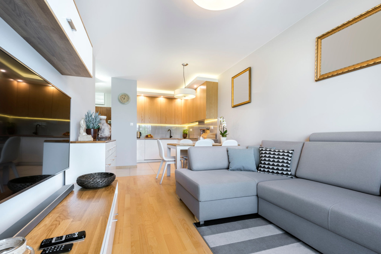 Sala con sofá esquinero gris, comedor integrado y cocina de diseño moderno con iluminación LED indirecta – FRANCO HomeServices