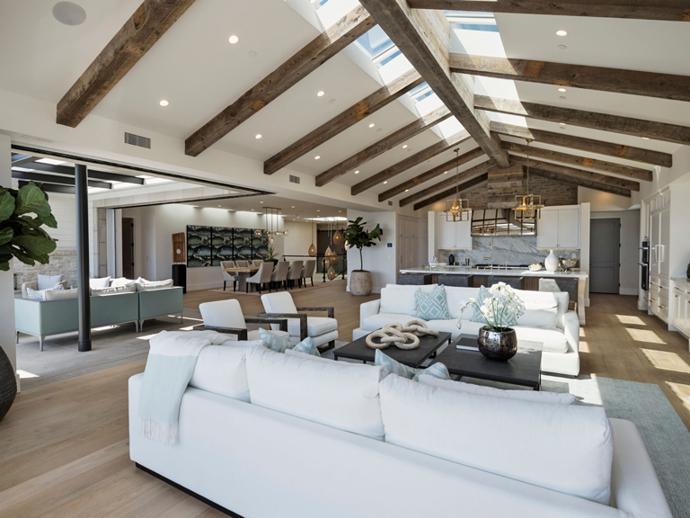 Sala, comedor y cocina integrados en un espacio abierto con techo alto, vigas de madera expuestas y abundante luz natural – FRANCO HomeServices